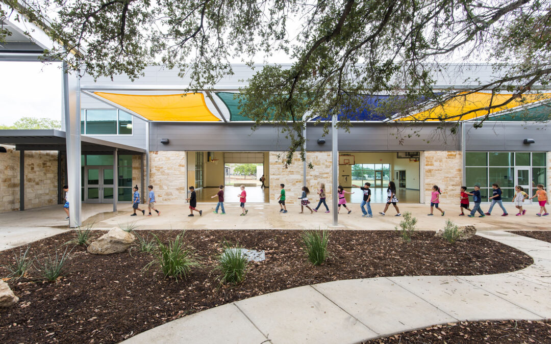 Children walk in a line under a color, green, and blue awning in front of the Lytle Elementary gym