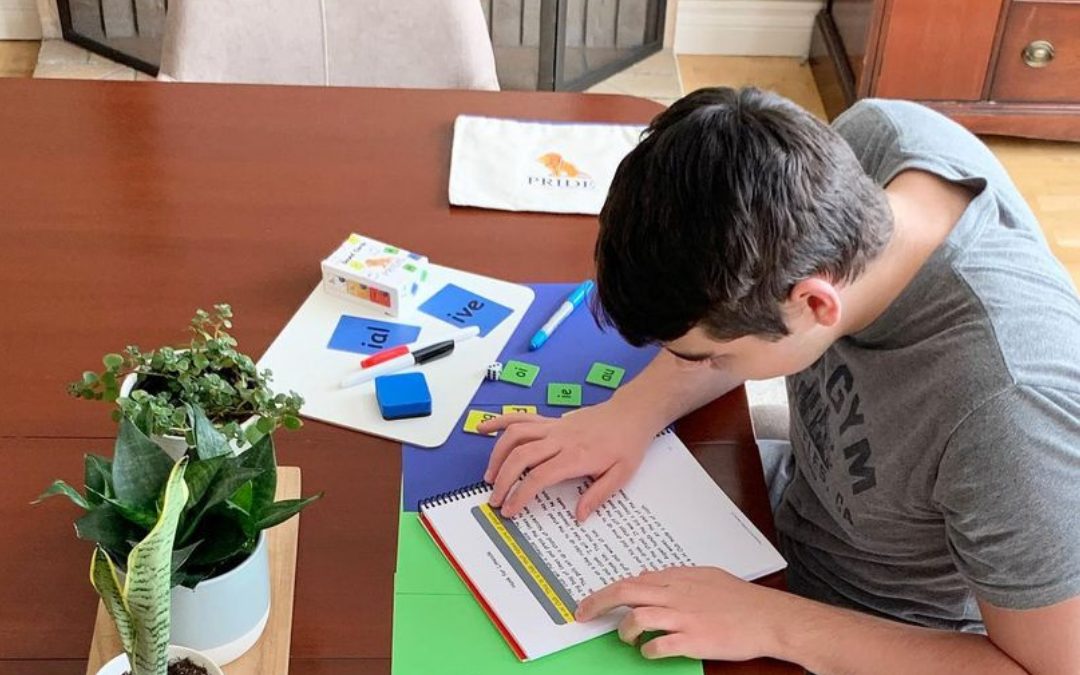 A teenage boy sits at a table and reads a PRIDE Reading Program passage using a tracker.